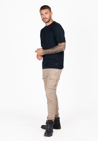 Czarny t-shirt krótki rękaw z okrągłym dekoltem, uzupełniony beżowymi spodniami cargo z wieloma kieszeniami oraz czarnymi sznurowanymi butami.