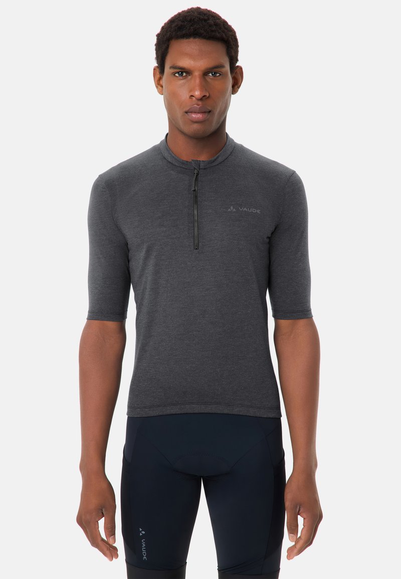 Modèle masculin portant un maillot de cyclisme à manches courtes gris foncé avec une fermeture éclair à mi-hauteur et un short de cyclisme rembourré noir, sur un fond uni.