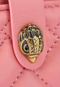 Cuir matelassé rose avec un embellissement en métal en forme de hibou doré et noir orné de petits studs ronds sur une sangle repliée.