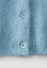 Tessuto morbido e peloso di colore azzurro chiaro con due bottoni tondi blu, che mostrano i dettagli della maglia testurizzata e dei bottoni.