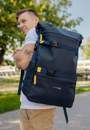 Navy blue roll-top backpack with yellow accents. Features adjustable straps, a top handle, and multiple zippered pockets for storage.