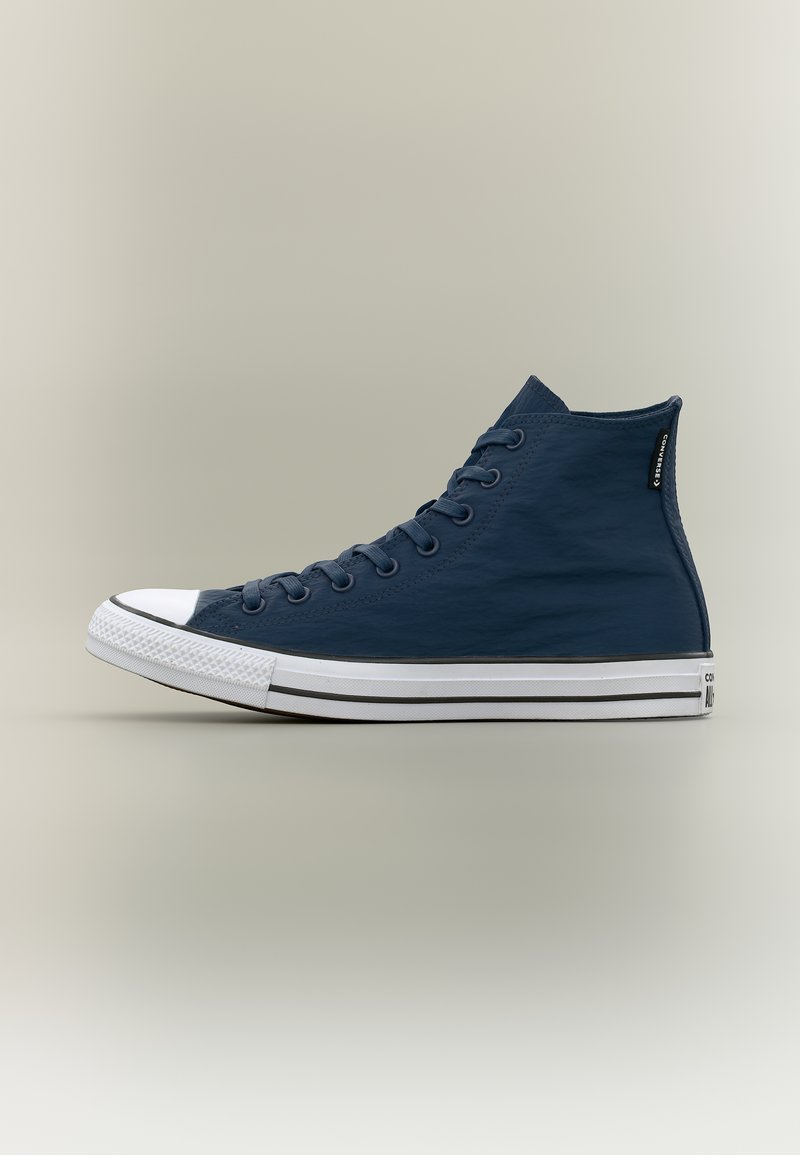 Μπλε ναυτικό ψηλό αθλητικό παπούτσι Converse με λευκή λαστιχένια σόλα, λευκό κάλυμμα μύτης και μαύρες ρίγες στη σόλα, εμφανίζεται από το πλάι.