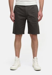 Pantalones cortos gris oscuro de algodón, con un diseño de frente plano, trabillas para cinturón y bolsillos laterales. Combinados con zapatillas altas blancas.