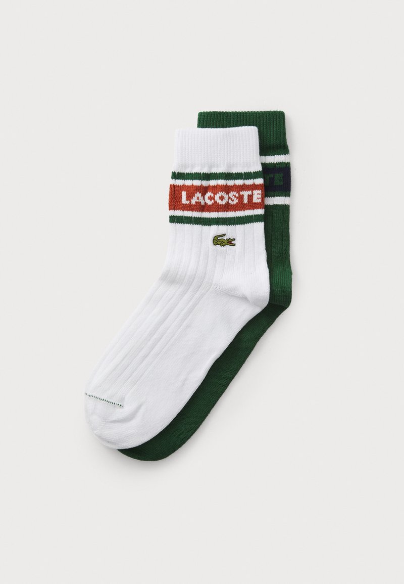 Meias de algodão com cores branca e verde, textura canelada, logótipo vermelho "LACOSTE" e pequeno emblema de crocodilo verde.