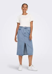 Jupe en denim avec une fente avant, lavage bleu et poches latérales. Associée à un t-shirt blanc uni et des baskets blanches. Texture lisse.