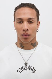 Hvit T-skjorte med svart "Ed Hardy" logo, sølvkjede med hjertet pendant, fremtredende tatoveringer av en rose og en sommerfugl på halsen.
