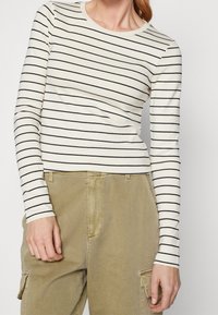 Långärmad krämfärgad topp med svarta horisontella ränder; mjukt tyg; figurn ära design. Matchad med ljus olivgrön cargobyxor.