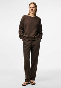 Sudadera marrón con mangas largas y cuello redondo, combinada con pantalones de corte holgado a juego. Textura suave, diseño minimalista, sandalias planas.