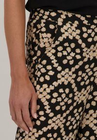 Zwarte broek met een beige abstract patroon, gemaakt van een gladde stof. Zijsokken zijn zichtbaar, met een rechte pijpdesign.