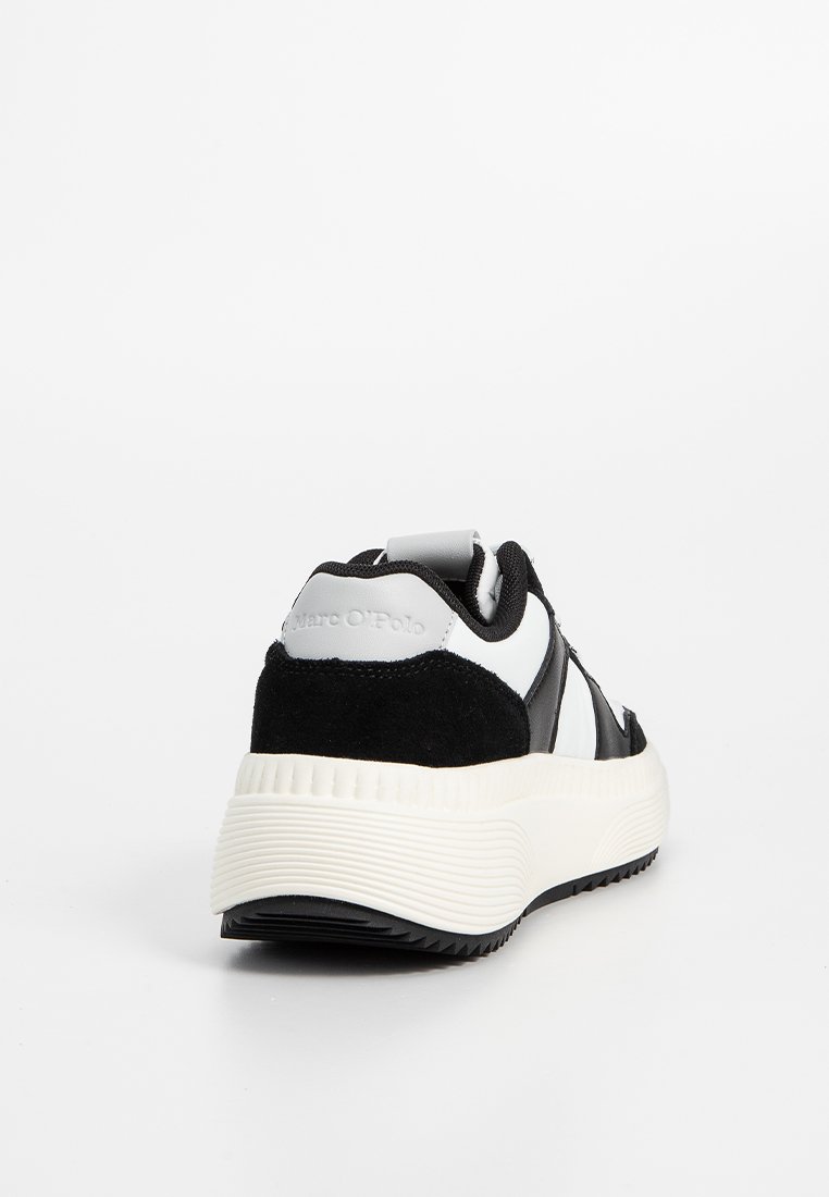 Schwarz-weißer Sneaker mit Obermaterial aus Veloursleder und Stoff, ausgestattet mit einer strukturierten weißen Sohle, Logo auf der Rückseite und einem gepolsterten Kragen für zusätzlichen Komfort.