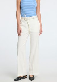 Krémové kalhoty s širokými nohavicemi, se stažením v pase a hladkým povrchem, v kombinaci s černými plochými botami.