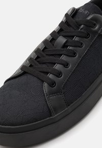 Svarta sneakers med en ovandel av kanvas och texturerad design, syntetiska l äderdetaljer, rund tå och platta skosnören. Gummisula.