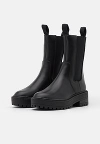 Black ankle boots with a smooth leather finish, elastic side panels, and pull tabs. They feature a chunky platform sole with deep treads.