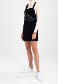 Abito da salopette in corduroy blu navy con due tasche frontali, abbinato a un dolcevita bianco e sneakers bianche con cinturino. Inclusa borsa a tracolla nera.