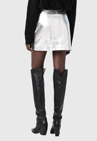 Melni ādas zābaki līdz ceļiem ar biezām papēžiem, augšdaļā ar šķēluma dizainu un gludu virsmu. Redzama sudraba mini svārku daļa.