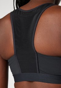 Sutiã desportivo preto com um design elegante, apresentando uma textura suave, alças largas e um recorte nas costas para ventilação e conforto.