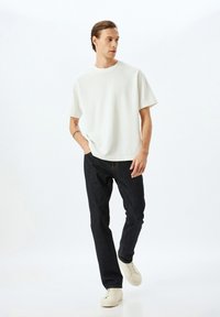 Hvid bomulds T-shirt med korte ærmer, parret med mørke denim jeans. Modellen bærer lyse sneakers. Enkel og moderne design.