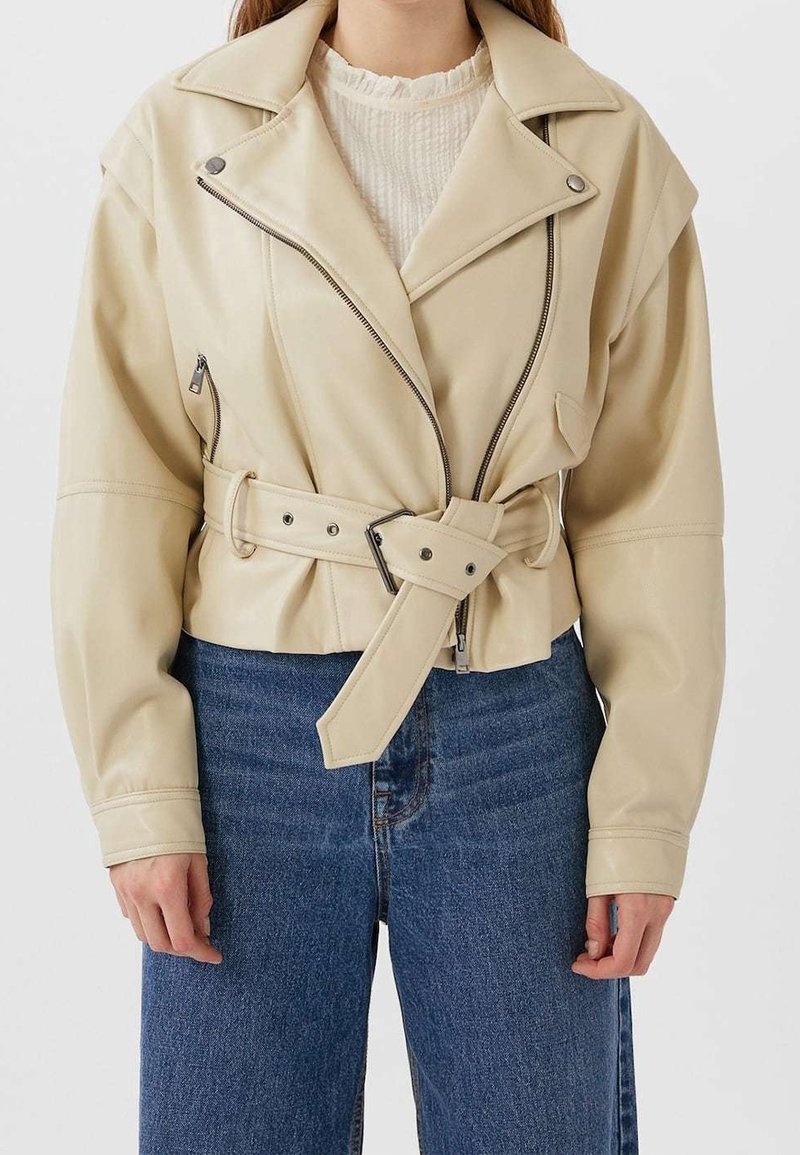 Crème faux leren cropped jack met verlaagde schouders, ritssluiting aan de voorkant, twee zijzakken en een ceintuur in de taille. Gepaard met hooggetailleerde blauwe jeans.
