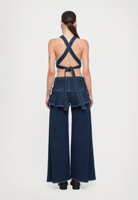 Denimu tērps ar krustu mugurā valkātu halter topu un platām biksēm. Zila auduma, viļņotas šorti jostas vietā un sasienama detaļa aizmugurē.
