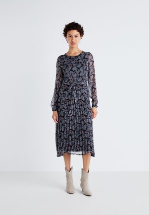 Robe à manches longues à motifs floraux sombres, avec une taille cintrée, une jupe plissée et des manches semi-transparentes. Association avec des bottes chevilles gris clair.