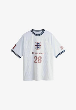 Fehér angol futballmez tengerészkék szegéllyel, három kék oroszlán címer, 26-os szám és „FIFA World Cup” a vállán.