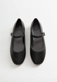 Svarta läderskor av typ Mary Jane med platt sula, rund tå och ett smalt band över insteget. Har en slät textur och minimal design.