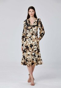 Robe florale en beige et noir avec de longues manches bouffantes, un col froncé et un ourlet. Présente une taille marquée et des poches latérales.