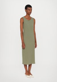 Rochie fără mâneci, din tricot ribetat de coloră verde măslinie, cu decolteu rotund, ajungând până la jumătatea gambei, având o siluetă ajustată și o textură moale.