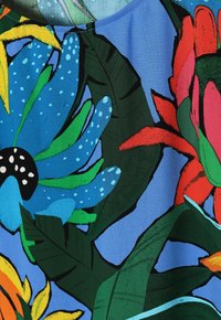 Tessuto floreale colorato con grandi fiori blu con accenti neri, foglie verdi e uno sfondo blu, che mostra vivaci motivi tropicali.