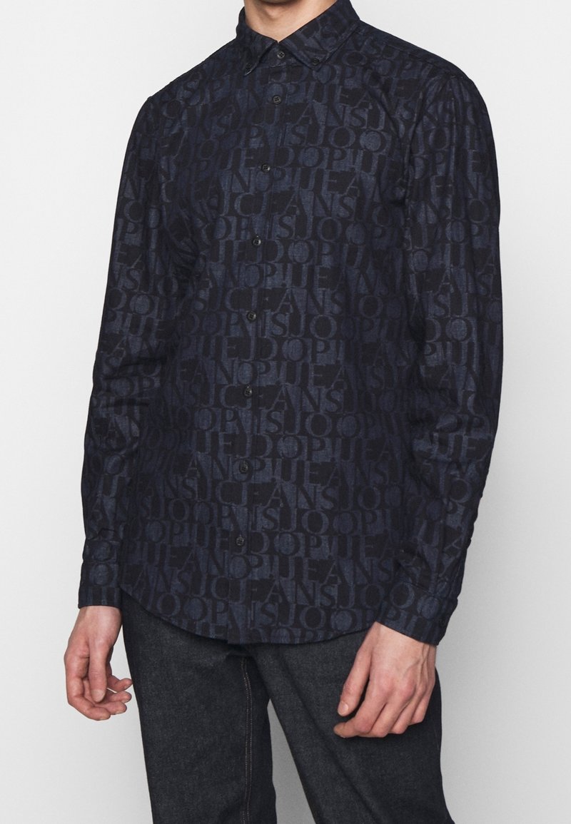 Camicia blu navy con bottoni, caratterizzata da un motivo testuale tonale, maniche lunghe e colletto strutturato, realizzata in un tessuto liscio.