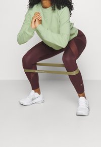 Sudadera verde, leggins burdeos con paneles de malla, hasta los tobillos, y zapatillas blancas con acentos plateados. Banda de resistencia colocada alrededor de los muslos.