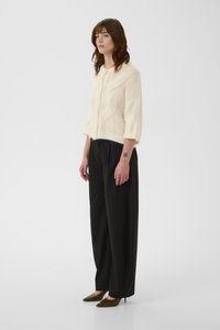 Ελεφαντόδοντο πλεκτό πουλόβερ με μανίκια μπαλόνι, υφασμένο σχέδιο· συνδυασμένο με μαύρο παντελόνι φαρδιάς γραμμής και πράσινα τακούνια με μυτερή μύτη.