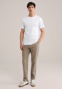 Tricou alb cu mânecă scurtă, asortat cu pantaloni scurți bej deschis și adidași bicolori. Material neted, croială casual și design basic.