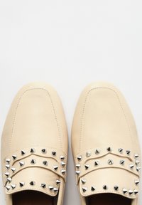 Mocassins en cuir beige avec deux rangées de clous pyramides argentés sur le devant, texture lisse, bout arrondi et design épuré.