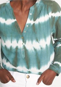 Maglietta a maniche lunghe, scollo a V, con motivo tie-dye verde e bianco. Caratterizzata da una chiusura con bottoni e tessuto testurizzato. Adatta per un look casual.