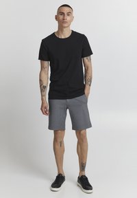 T-shirt en coton noir, col rond. Shorts gris avec une texture lisse, longueur au-dessus du genou. Baskets noires avec des semelles blanches.
