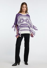 Poncho tricotat în nuanțe de violet și alb cu modele geometrice, margini ciufulite și o croială lejeră. Purtați cu pantaloni negri și botine cu toc.