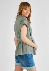Roheline lühikeste varrukatega topp peplum-mustriga, vöökoht ja kerge materjal, koos siniste denim lühikeste pükstega, mille käised on rullitud.