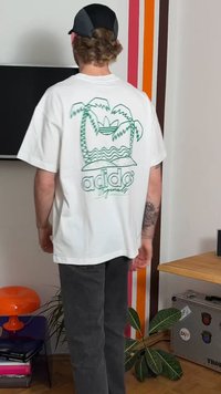 Balta T-krekls ar zaļas palmas koka un vilnis grafiku, uz kura redzams teksts "adidas Originals", kombinēts ar tumši pelēkām biksēm.