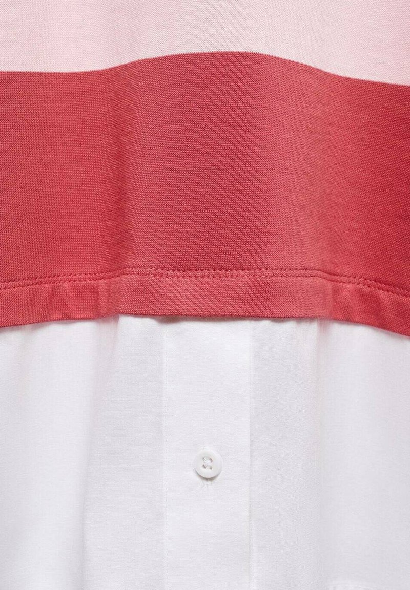 Top a righe rosso e rosa chiaro con una sezione di camicia bianca sottostante. Tessuto di cotone morbido con una consistenza liscia e un dettaglio con un solo bottone bianco.