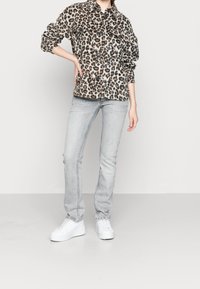 Lepardmönstrad jacka med knäppning, kombinerad med ljusgrå jeans och vita plattformssneakers. Outfiten har en avslappnad passform och texturerad tyg.