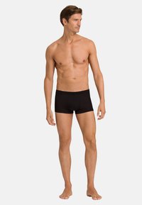 Černé pánské spodní prádlo vyrobené z hladké tkaniny, s pohodlným střihem a elastickým pasem, stylizované jako šortky typu trunk.