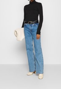 Czarny golf, jasnoniebieskie dżinsy z wysokim stanem i szerokimi nogawkami, czarny pasek z owalną klamrą, kremowa torebka z fakturą oraz beżowe klapki na obcasie.