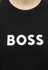 Μαύρο μπλουζάκι με λαιμόκοψη, με τη λέξη BOSS τυπωμένη σε μεγάλα λευκά κεφαλαία γράμματα στο στήθος.