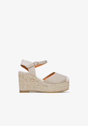 Sandale compensée beige au design espadrille, tige en tissu, bout rond, arrière ouvert et sangle de cheville avec boucle.