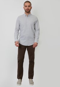 Camisa de botones gris claro, de manga larga, con tejido de mezcla de algodón, combinada con pantalones marrones y zapatos slip-on gris claro. Diseño simple y limpio.