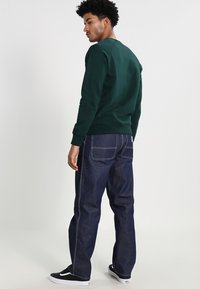 Green cotton sweatshirt, round neckline, ribbed cuffs, paired with dark blue denim jeans, straight leg, contrast stitching, classic back pockets.