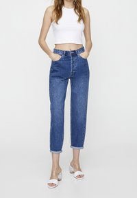 Höga blå denimjeans med avslappnad passform, med framfickor och uppvikta fållar, i kombination med vita sandaler med klara klackar.