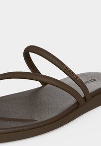 Καφέ σανδάλι Crocs με δύο λεπτά λουράκια, ανάγλυφη εσωτερική σόλα και ανάγλυφο λογότυπο Crocs στο επάνω λουράκι.