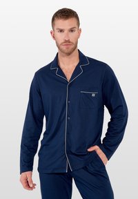Conjunto de pijama para hombre en azul marino, fabricado en tejido suave, que incluye una camisa con botones y ribete blanco, un bolsillo en el pecho y pantalones a juego.